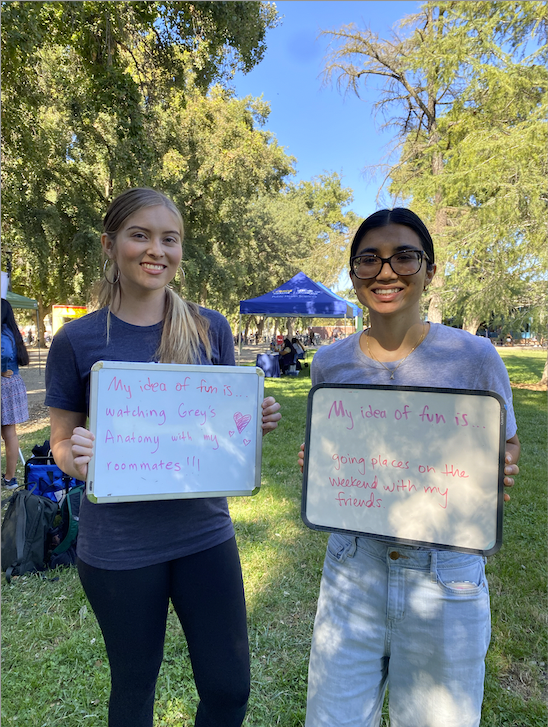 Two students holding signs that say "My idea of fun is" with "Going places on the weekend with my friends" and "watching Grey's Anatomy with my roommates" 